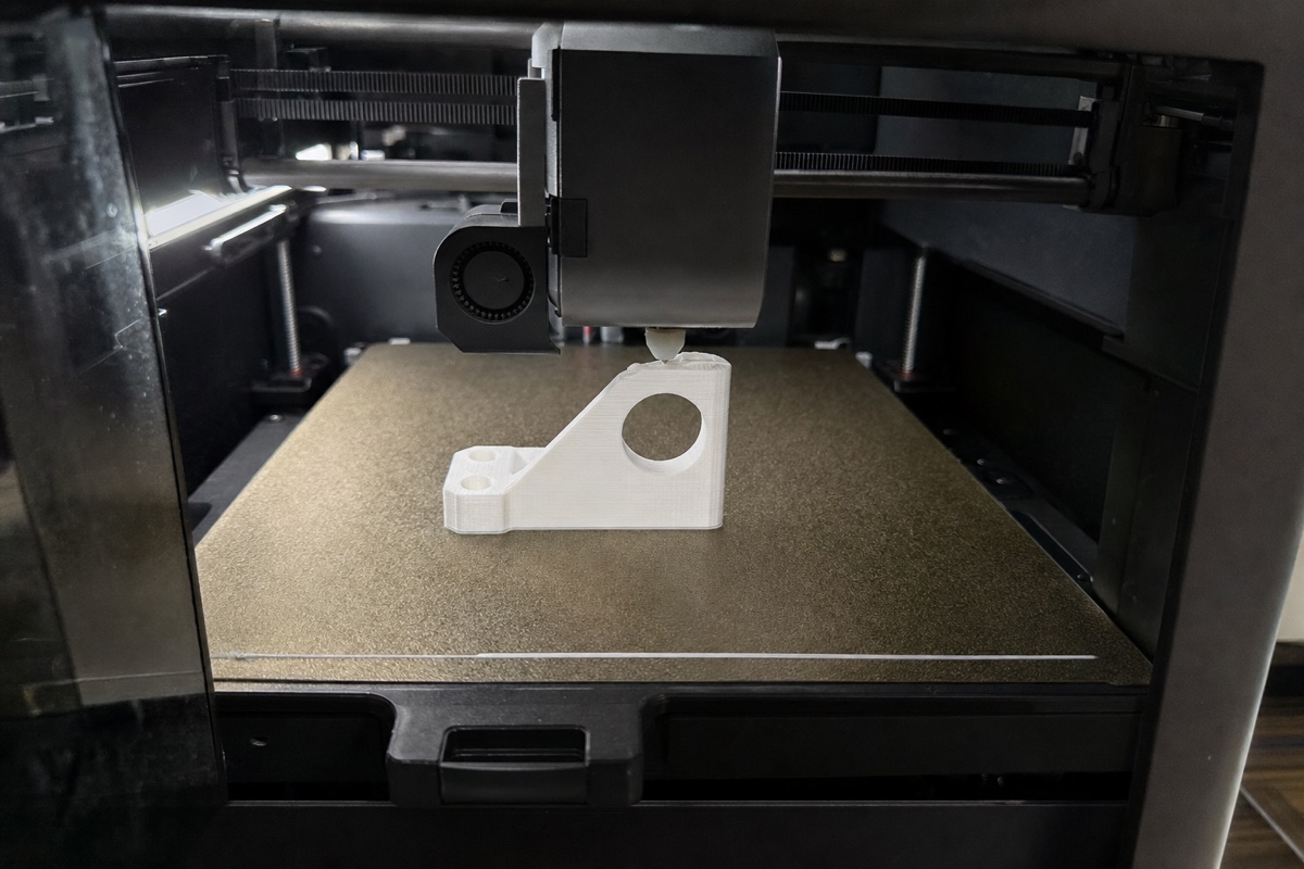 3Dプリンターの中で、ノズルが白い樹脂の糸を置きながら部品を積み上げている様子